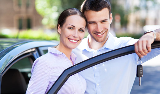 A young couple standing by their car. The main is holding keys to the car.